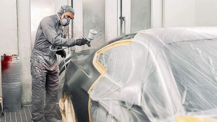 Lackierer mit Atemschutz bei der Lackierung eines sorgfältig abgedeckten Fahrzeugs